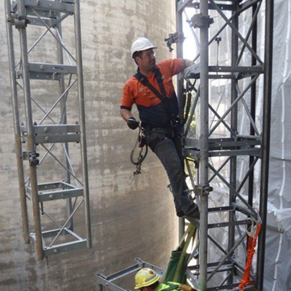 A man wearing a hard hat is standing on a scaffolding