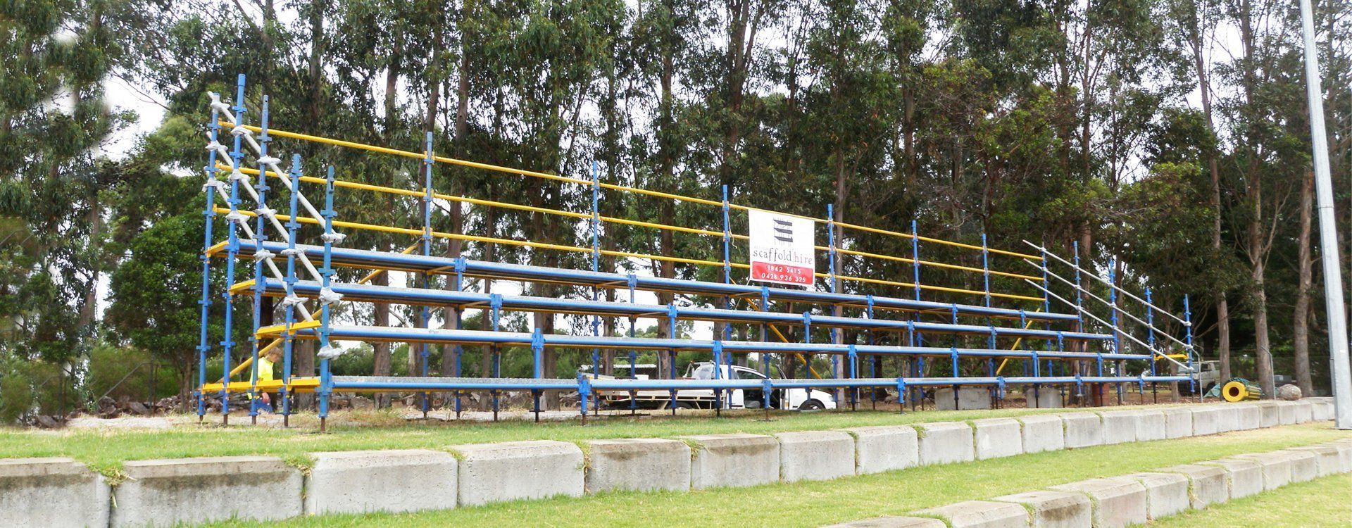A blue and yellow bleacher in a field with trees in the background.