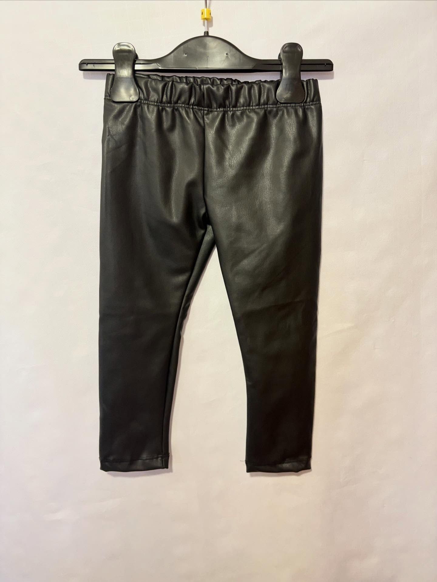 Pantaloni neri in finta pelle appesi a una gruccia nera.