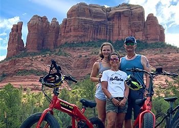 A group of people standing next to bicycles in front of a mountain.