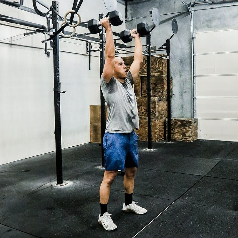A man is lifting dumbbells over his head in a gym