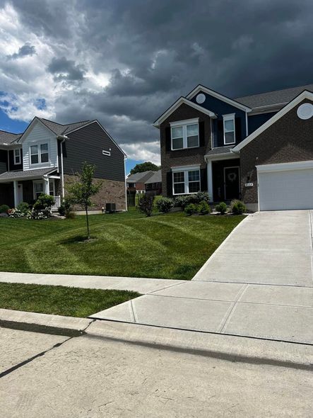 Two-story houses with green lawns under a cloudy sky. A driveway leads up to one house.