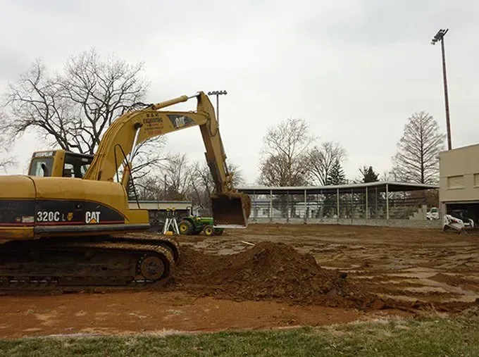 A large yellow excavator is digging a hole in a dirt field.