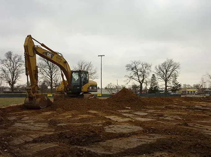A large yellow excavator is moving dirt in a field.