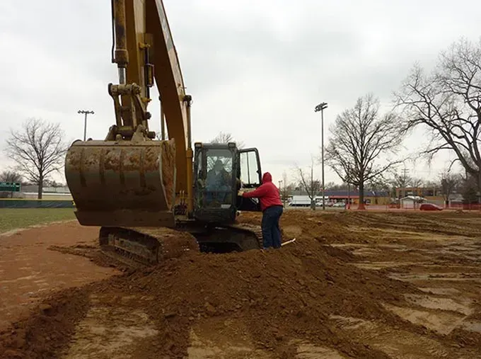 A man in a red hoodie is standing next to a large excavator.