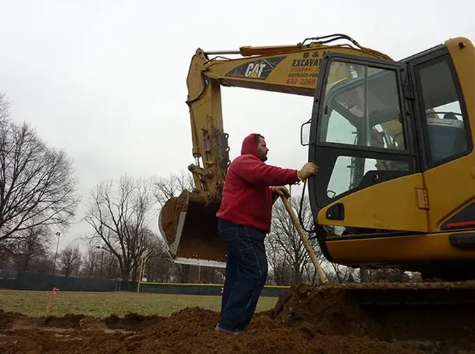 A man is standing in front of a cat excavator