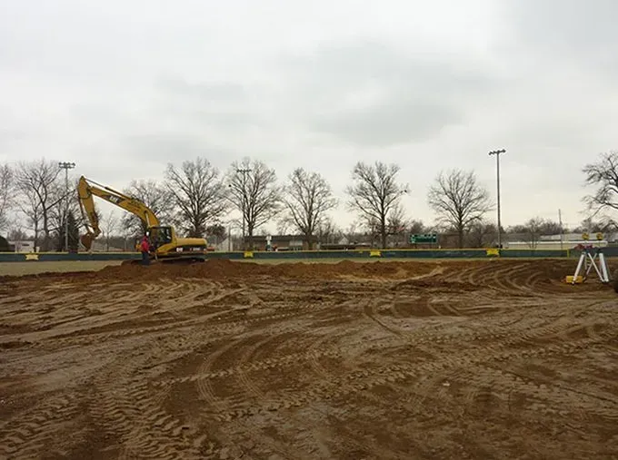 A large yellow excavator is digging a hole in a dirt field.