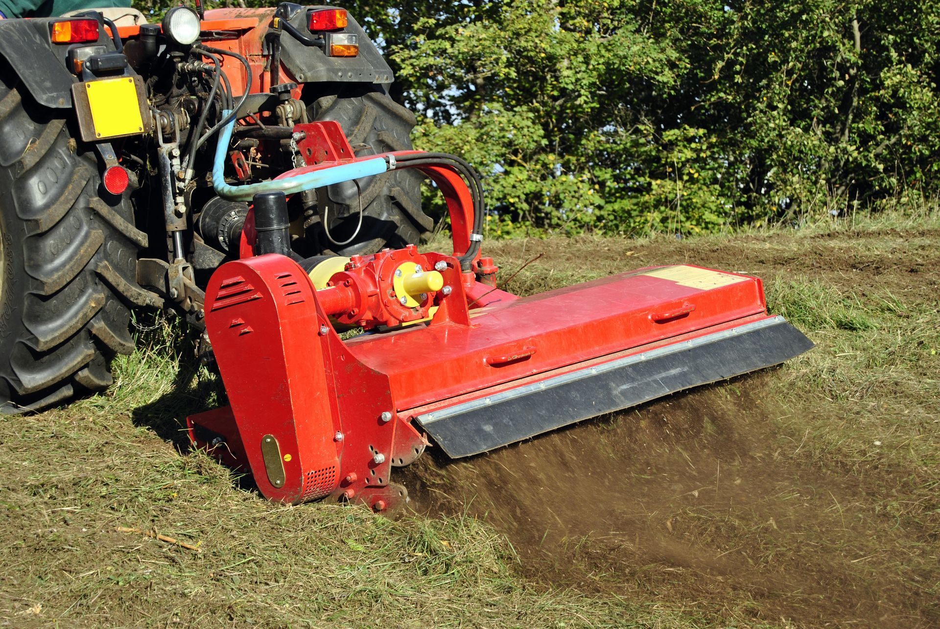 A red and black tractor is cutting grass in a field.