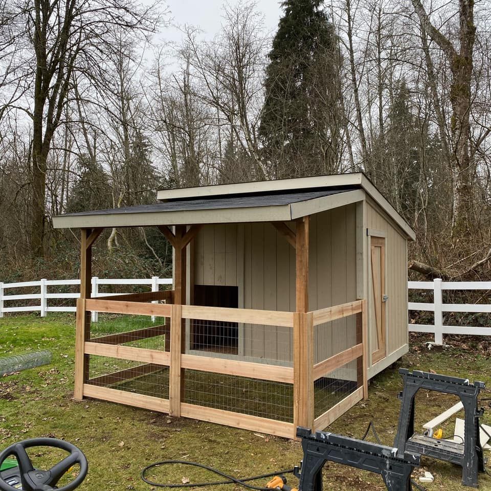 A chicken coop with an attached run, built with wood. It's tan and brown, with a white fence.