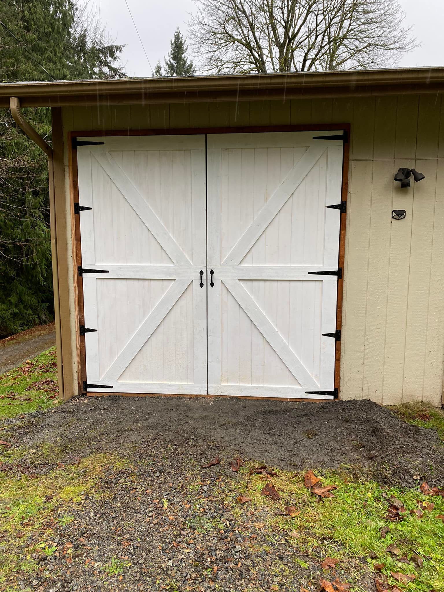 White barn-style double doors with black hardware, surrounded by brown trim, set in a light beige building.