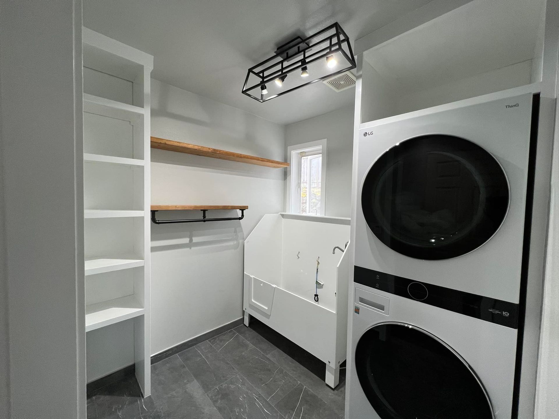 Laundry room with white cabinets, washer/dryer, dog wash station, and shelves. Gray flooring and walls.