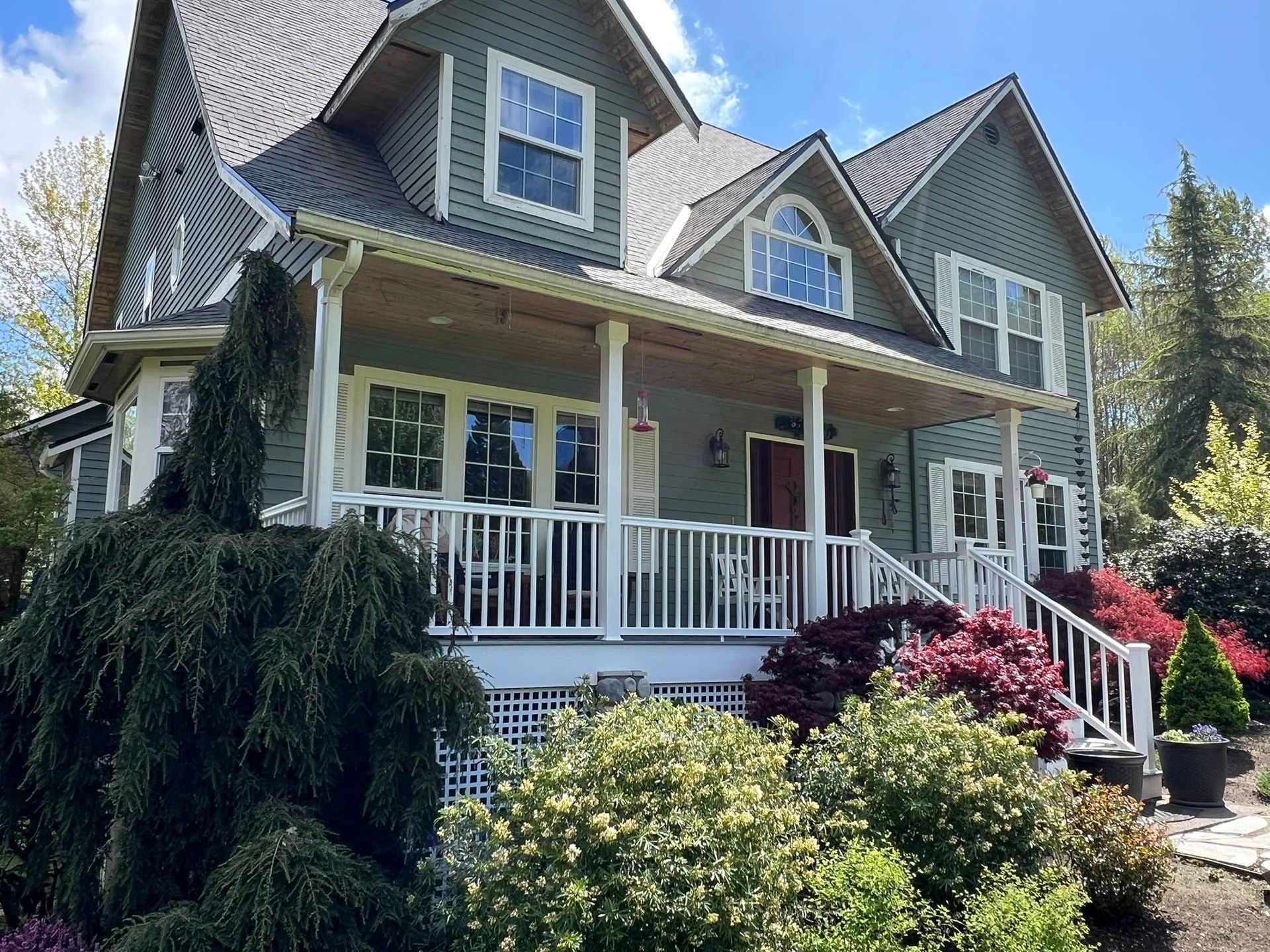 Green Victorian house with white trim, porch, and lush landscaping.