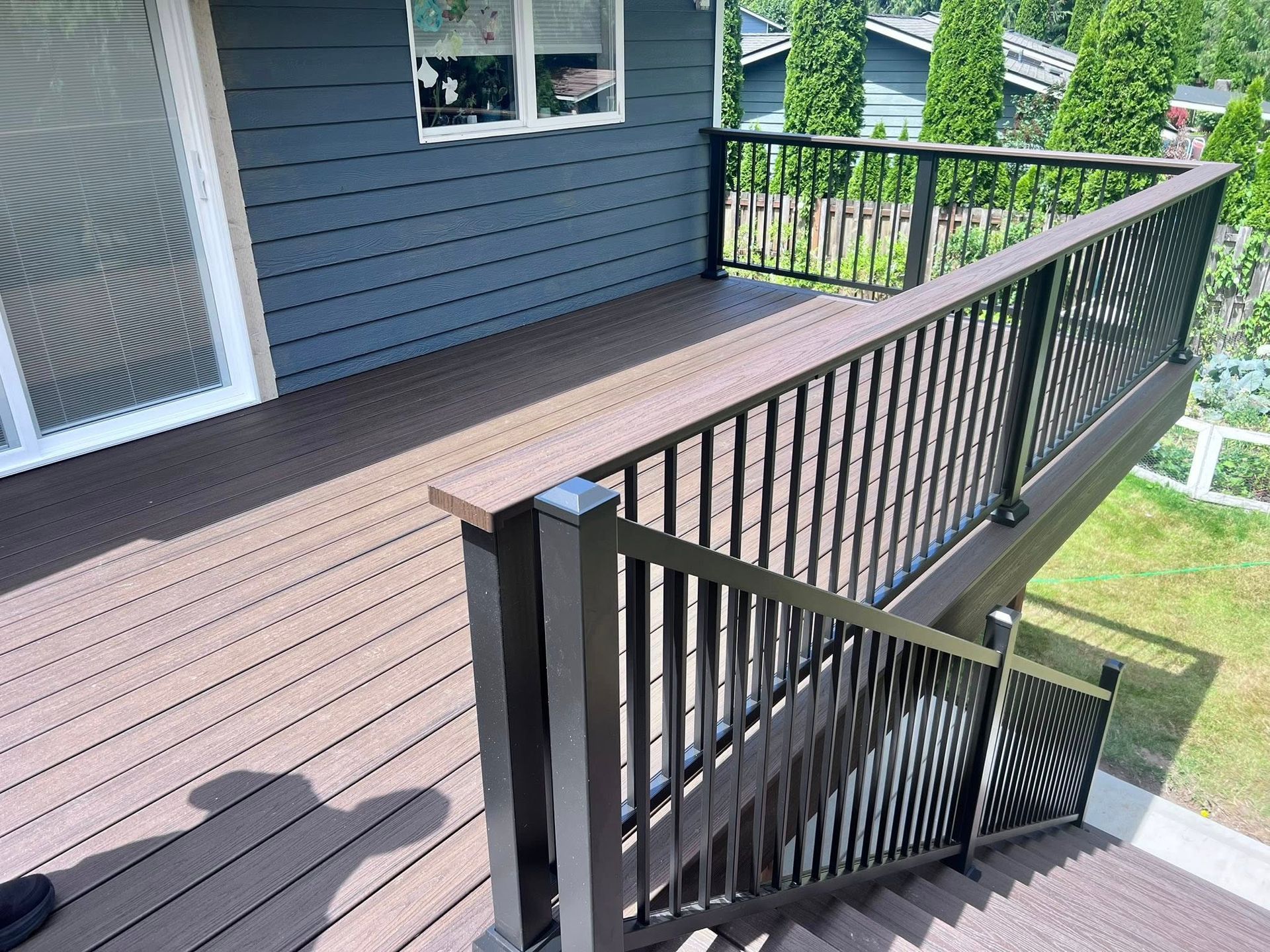 Brown deck with black railing and steps leading up to the house with blue siding.