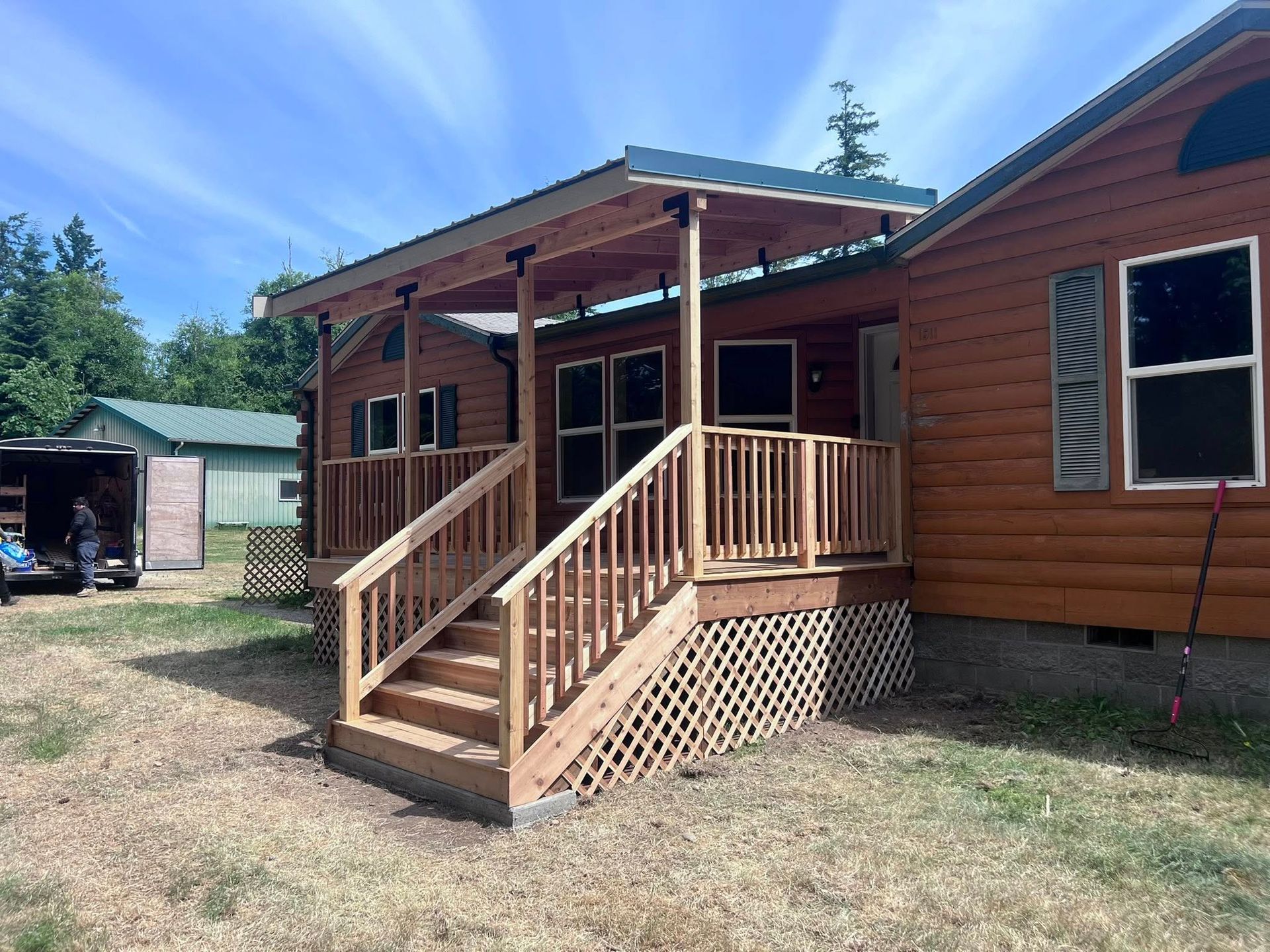 Wooden cabin with porch and stairs under a blue sky.