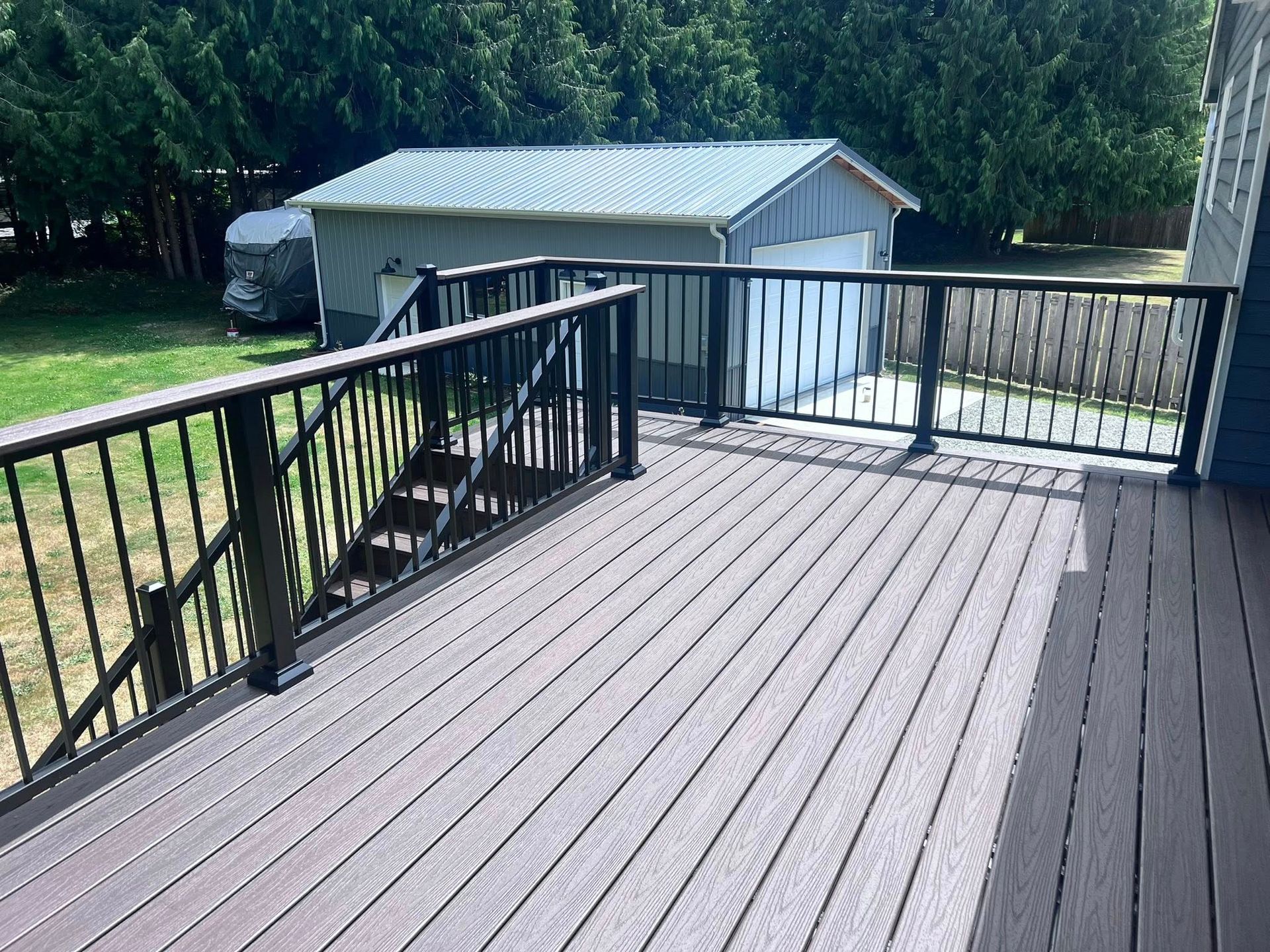 Wooden deck with black railing and steps, leading to a garage in the background.