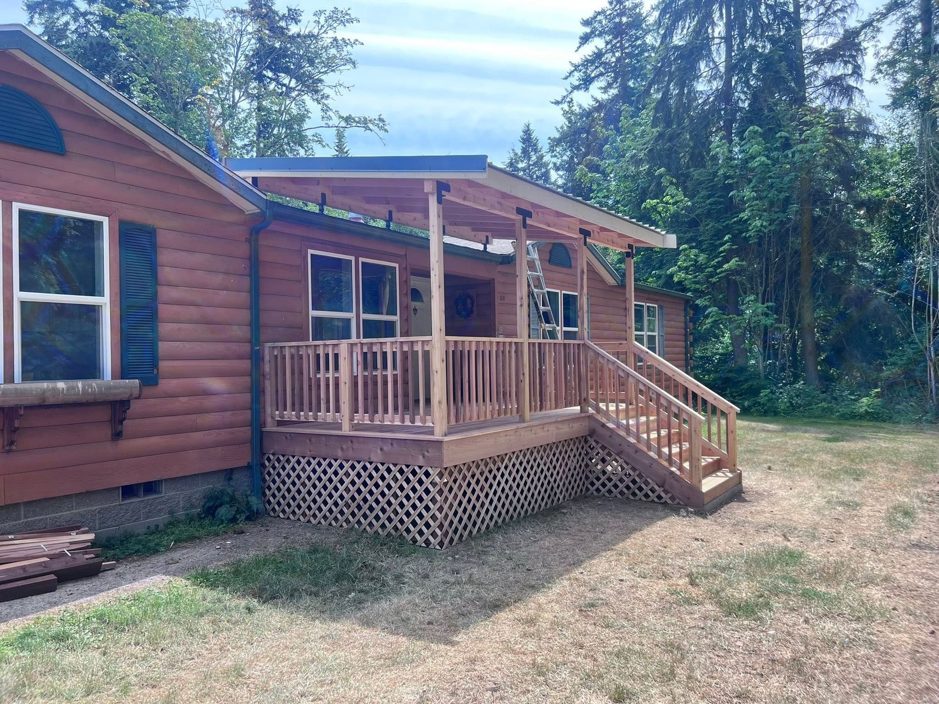 Brown cabin with wooden porch and railing, surrounded by trees.