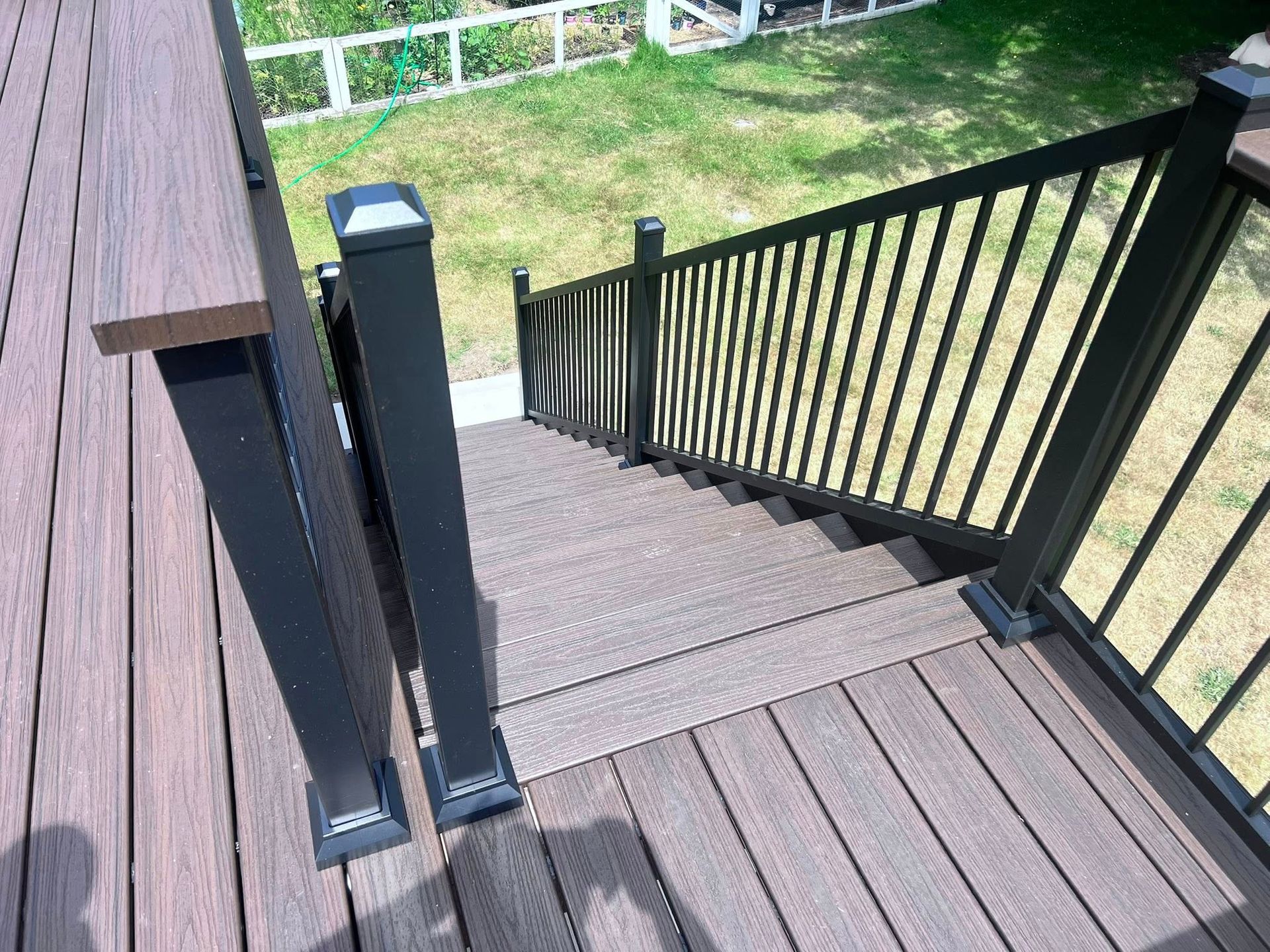 Outdoor deck with stairs, brown composite decking and black railing. Backyard view.