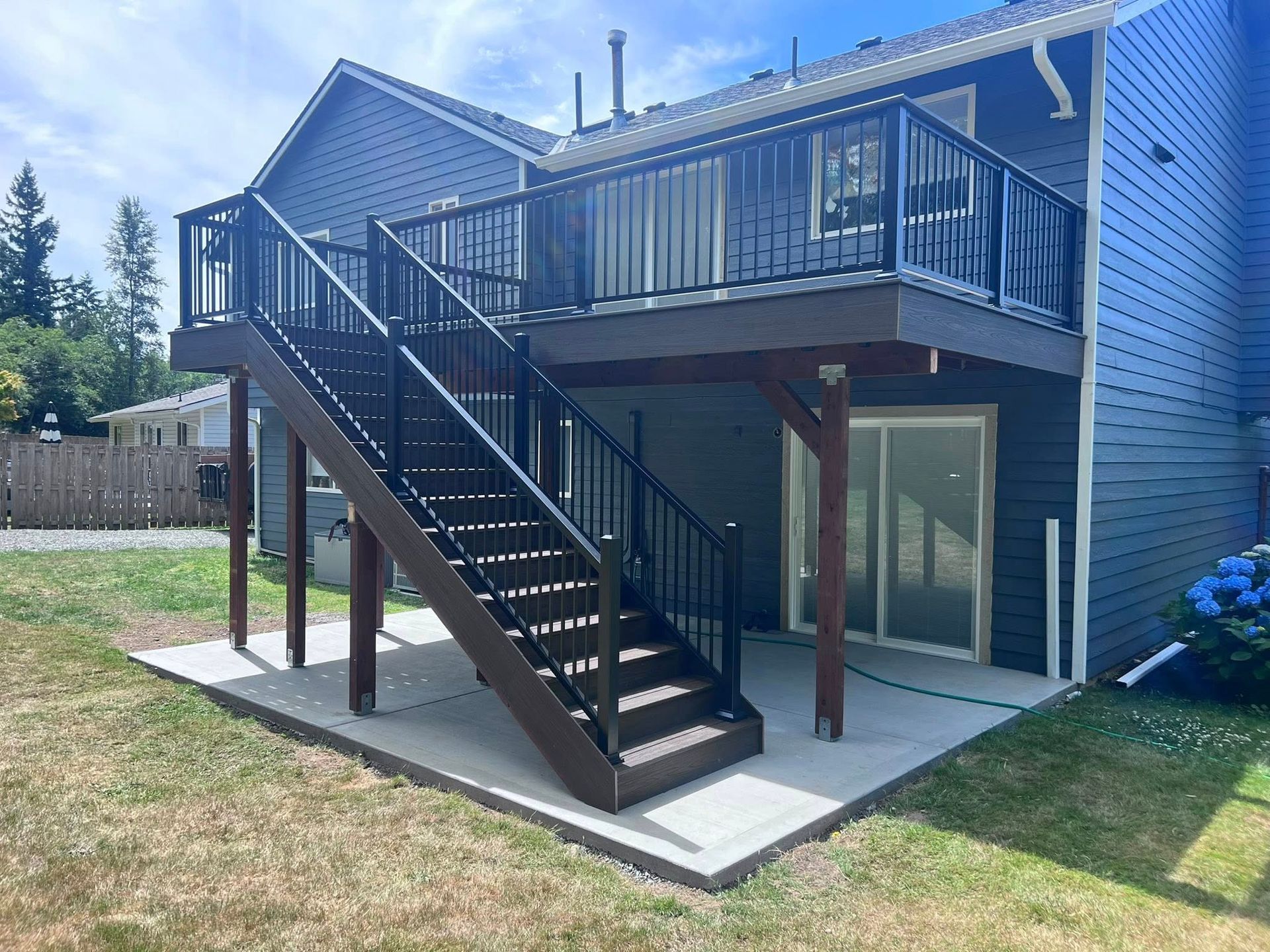 Deck with dark railings and stairs attached to a two-story house with gray siding.