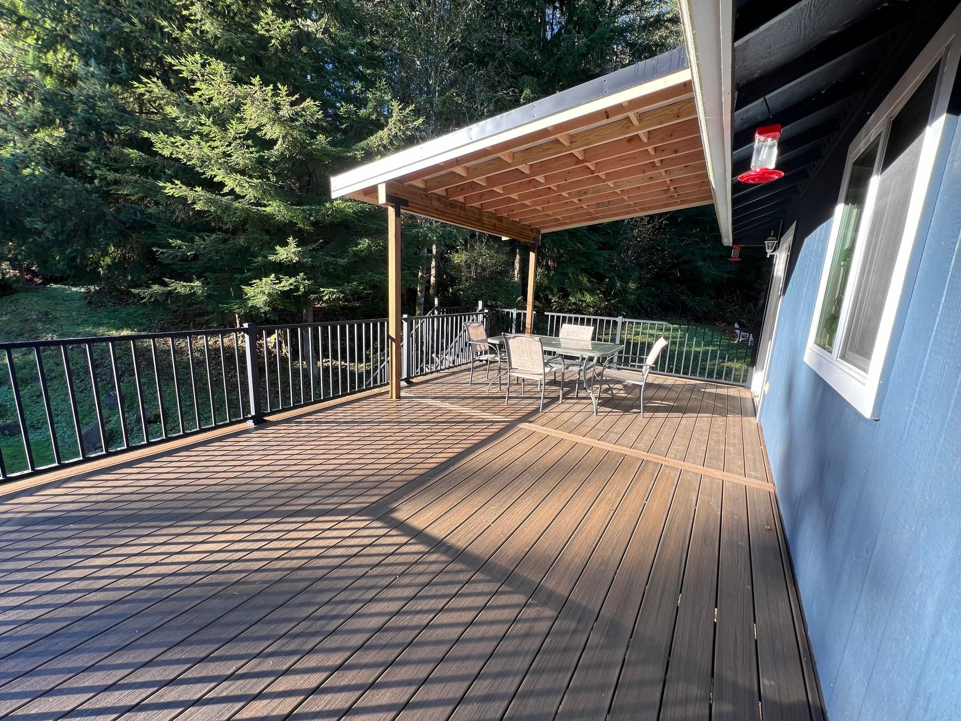 Wooden deck with a covered area, railing, and outdoor furniture. The house is blue.