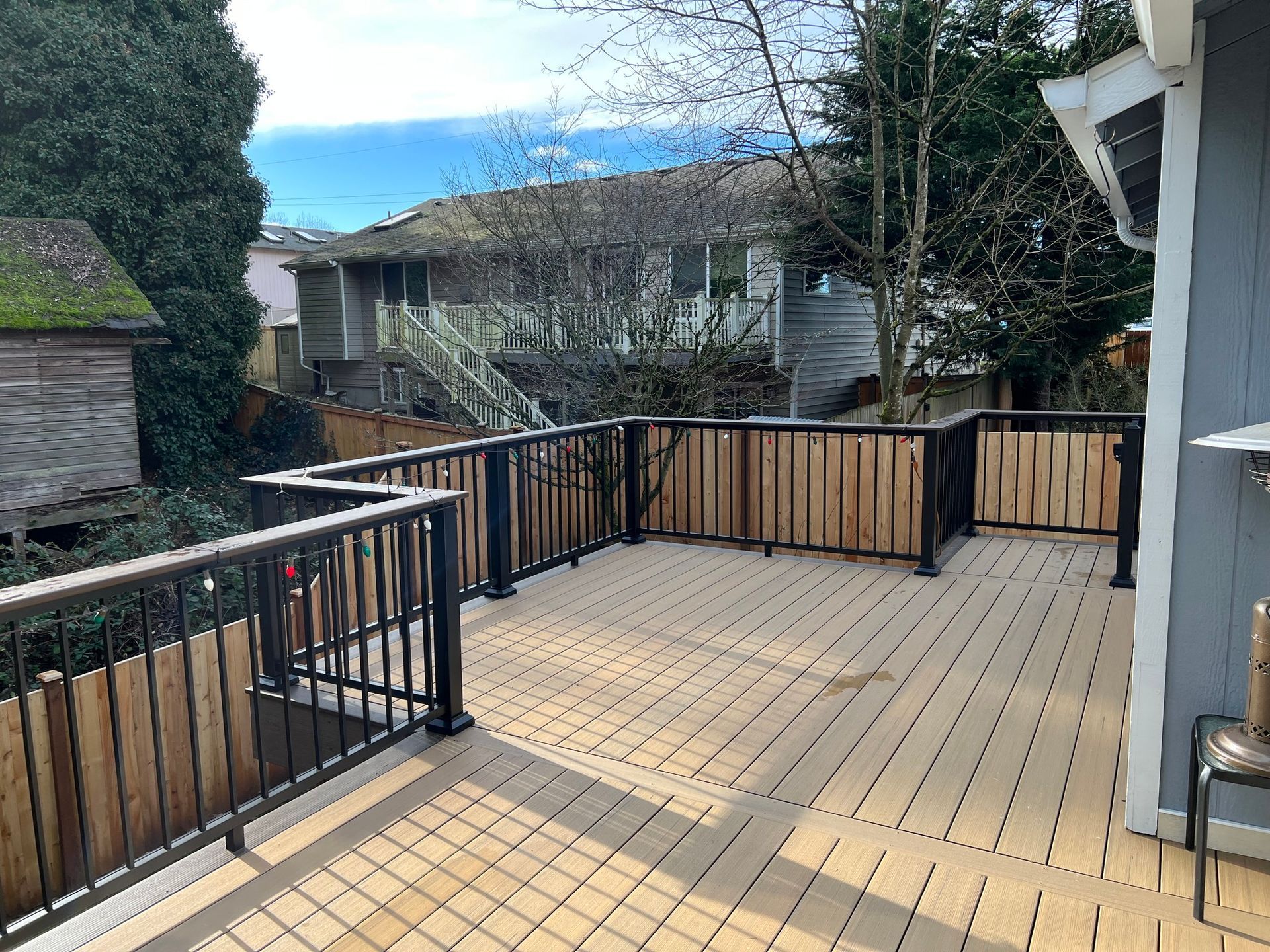 Wooden deck with black railings and wooden privacy panels, overlooking a residential backyard.