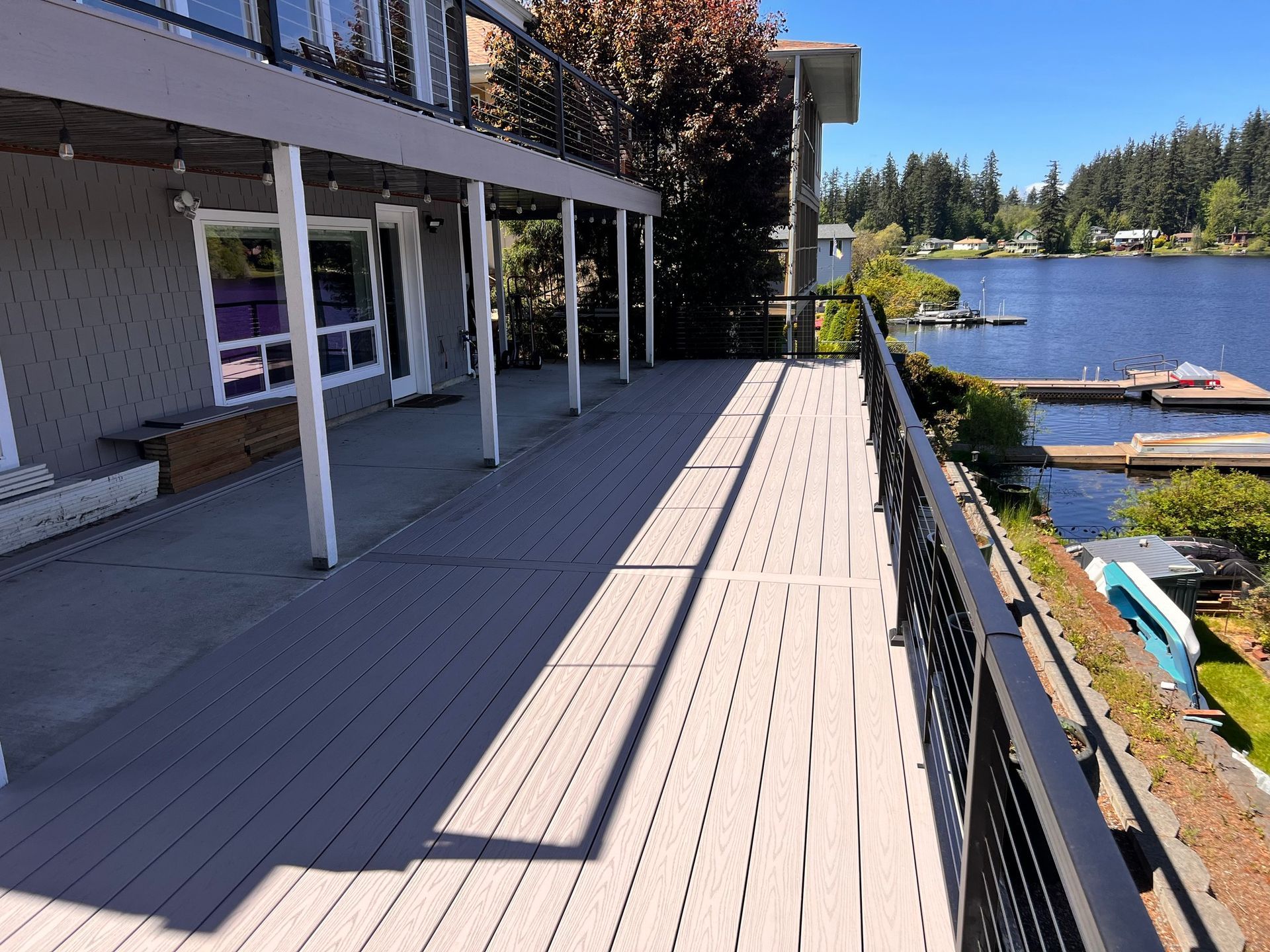 Wooden deck overlooking a lake with a house on the left and docks in the distance.