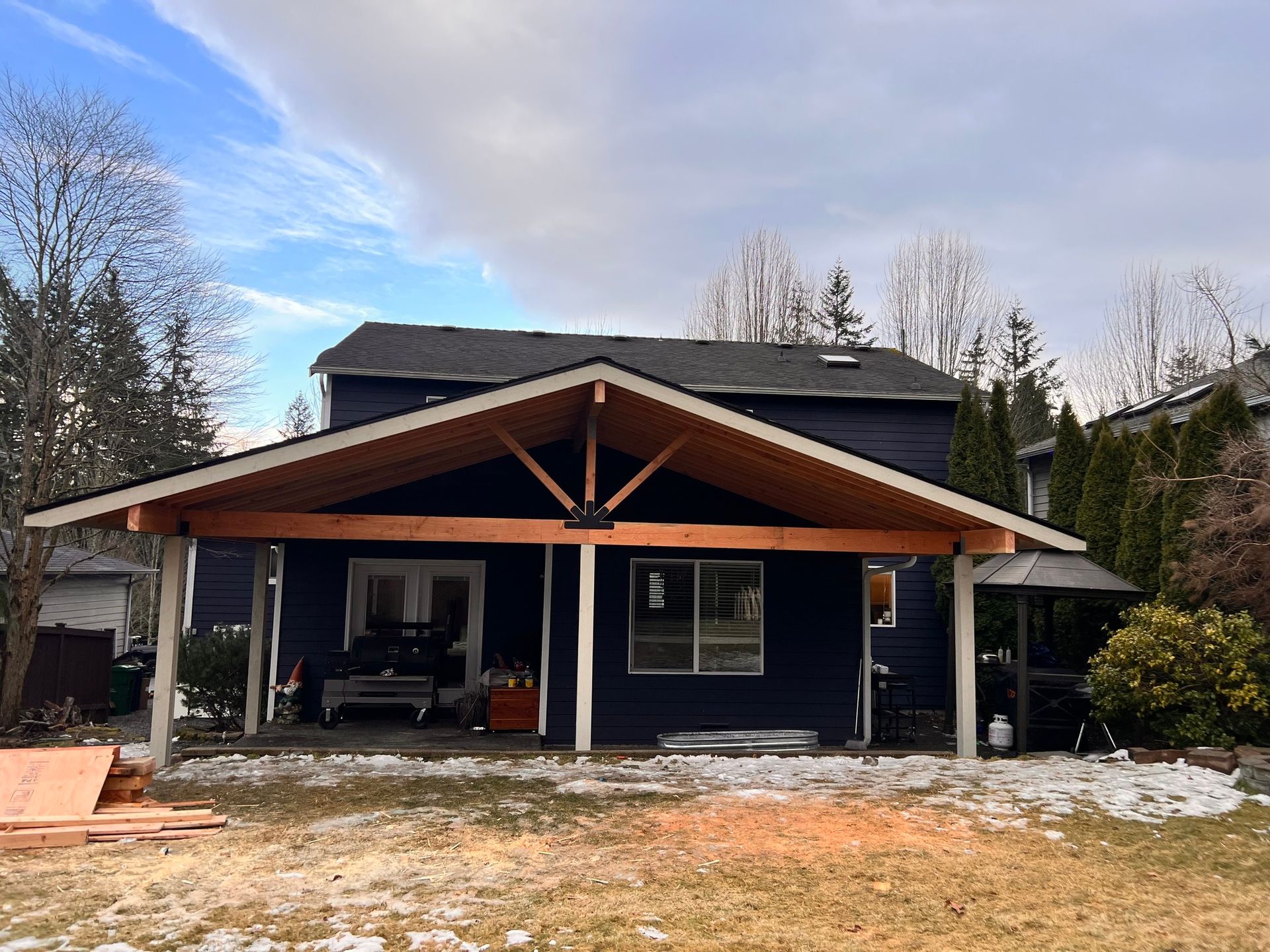A covered patio extension under construction, attached to a dark blue house.