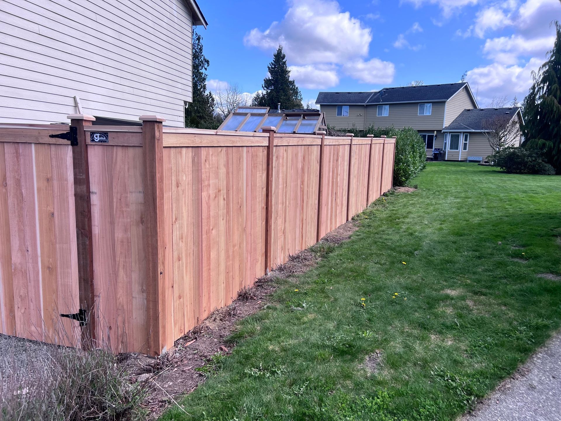 Wooden fence alongside a grassy lawn in a residential area. Sunny day, blue sky.