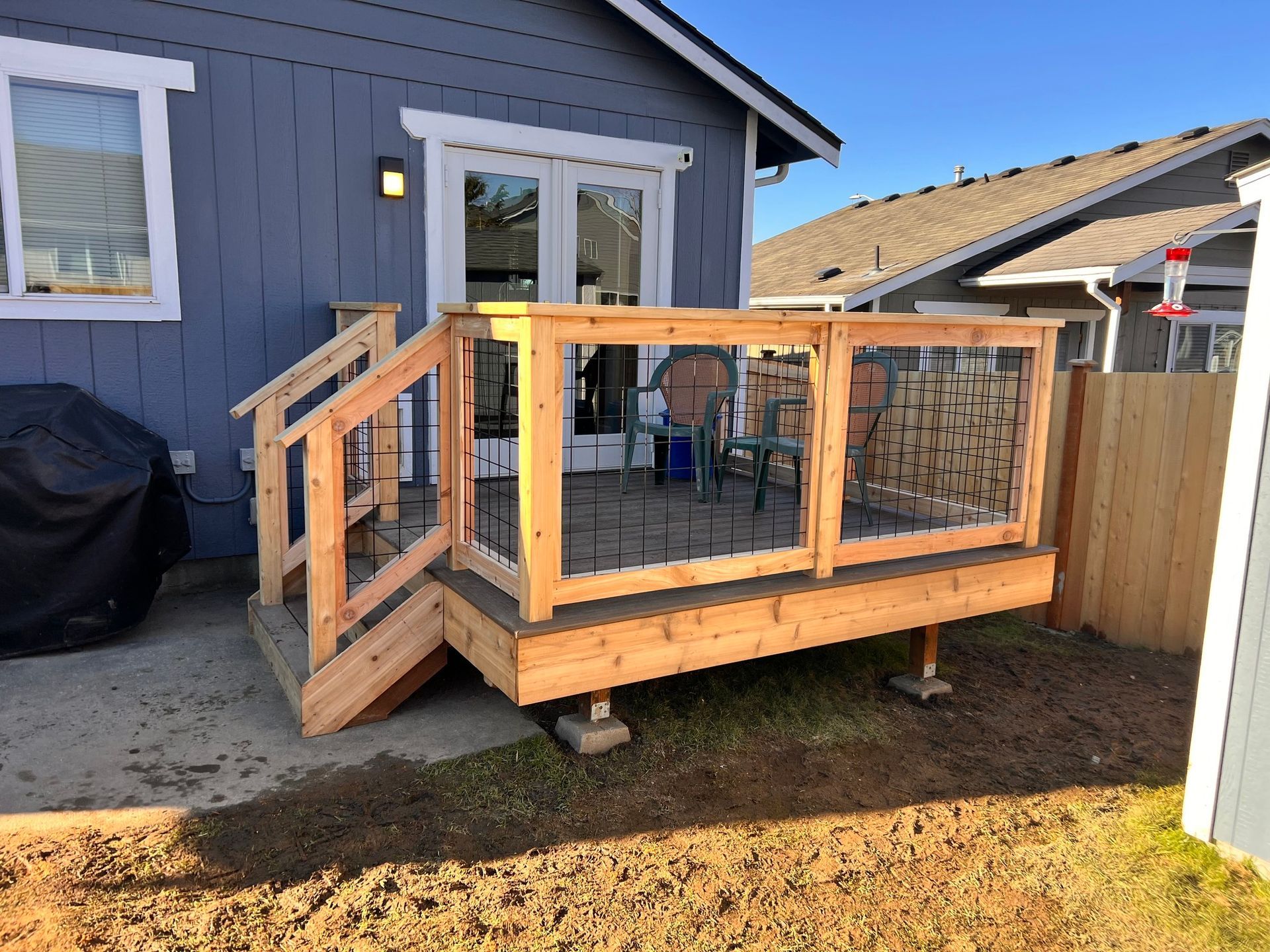 Wooden deck with wire mesh railing, attached to a blue house with French doors.