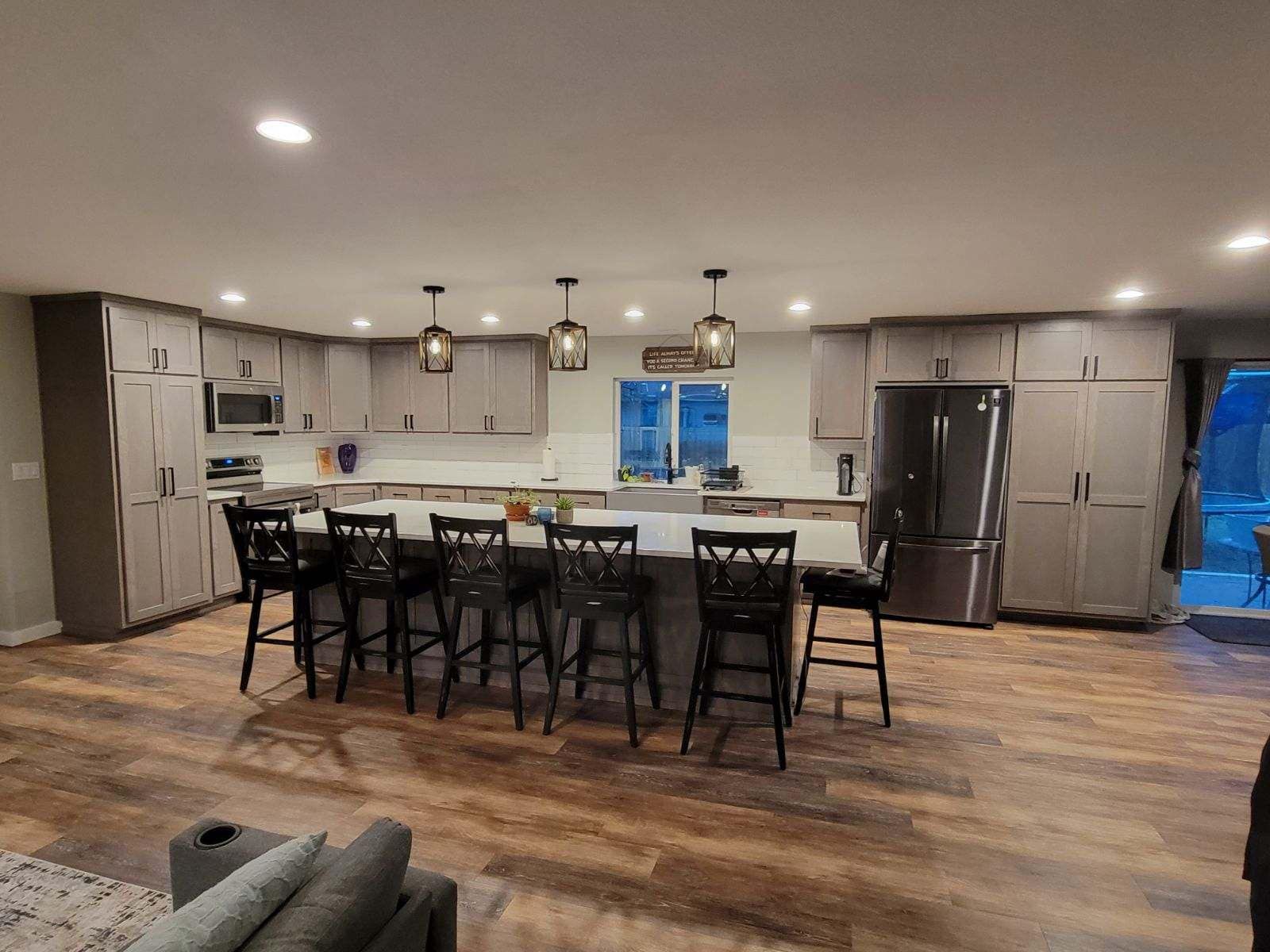 Kitchen with gray cabinets, large island with bar stools, stainless steel appliances, and wood-look flooring.