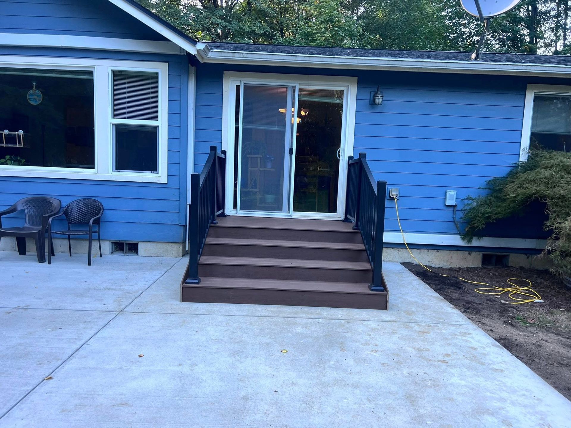 Blue house exterior with sliding door, deck stairs, and concrete patio. Two black chairs on the patio.