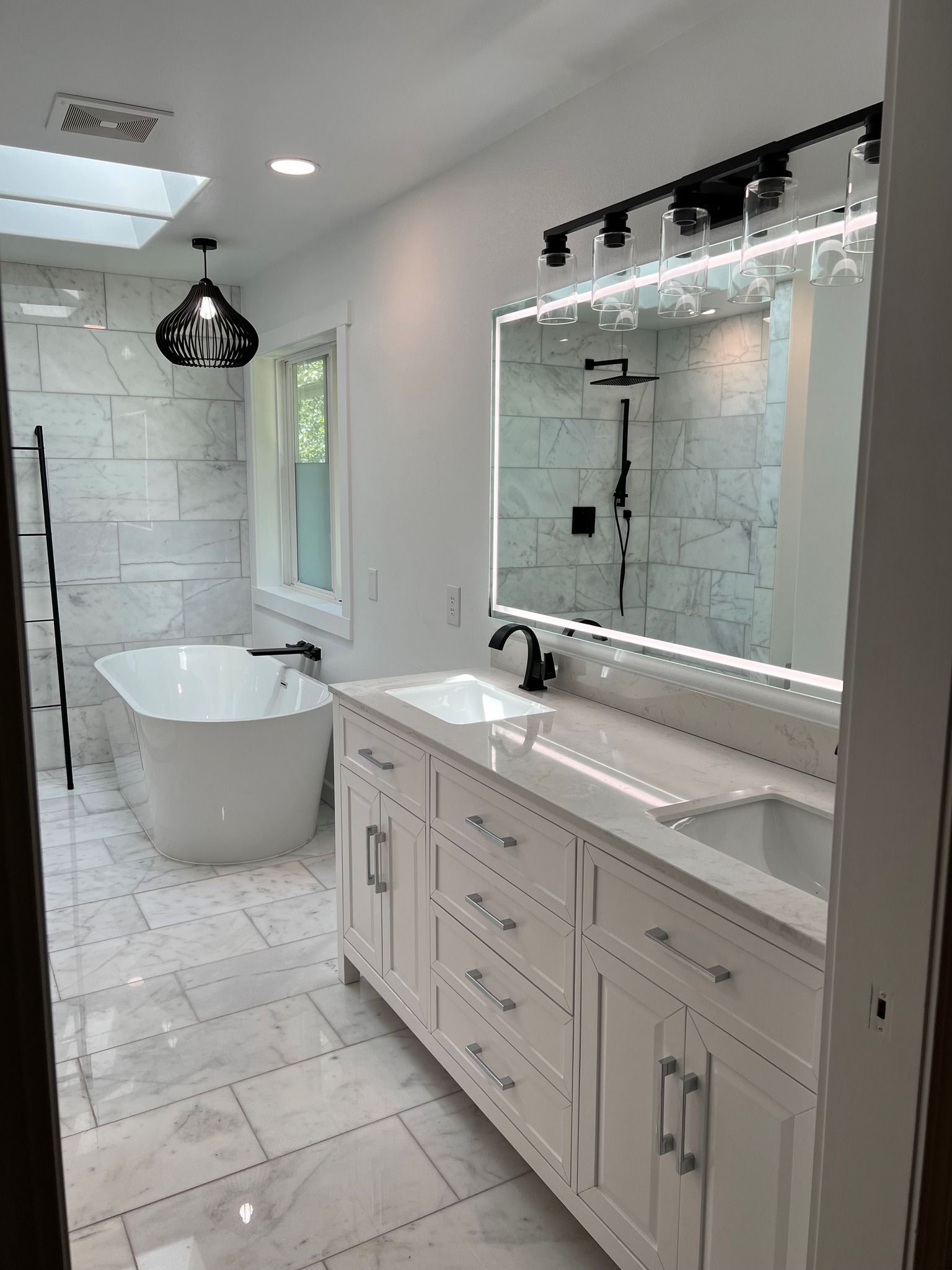 Modern white bathroom with freestanding tub, double vanity, and large mirror.