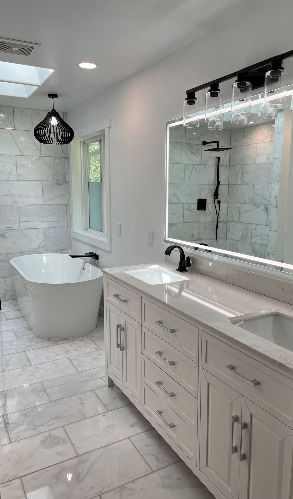 Modern white bathroom with a tub, double vanity, shower, and skylight.