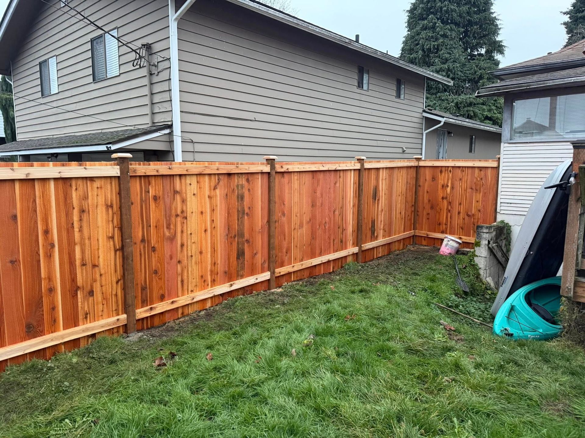 Wooden fence in a backyard with green grass and a house in the background.