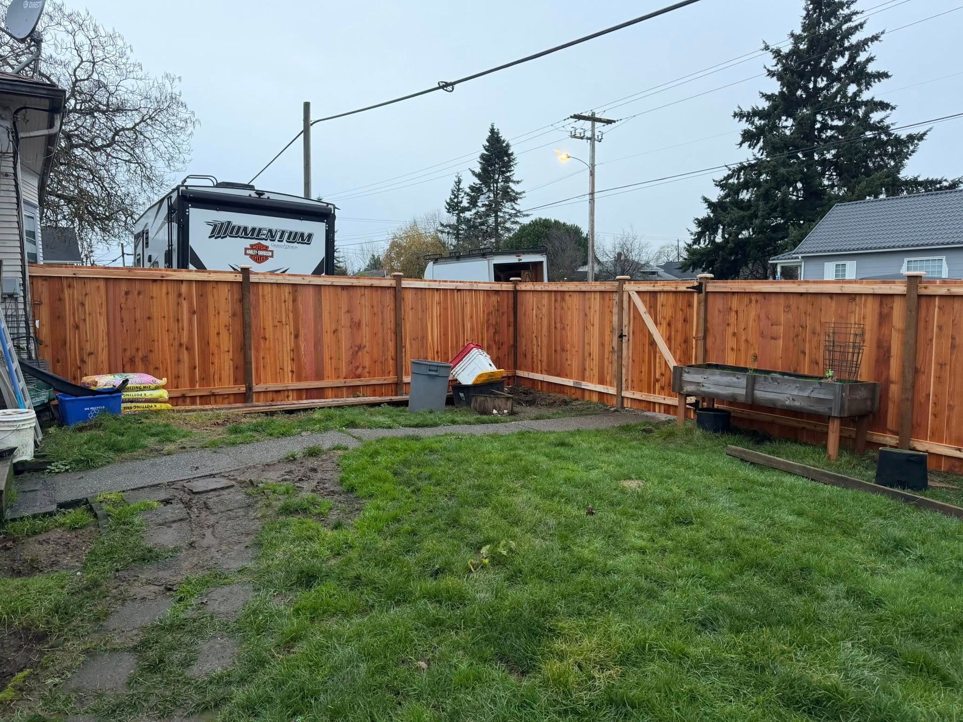 A new cedar fence surrounds a grassy backyard, cloudy sky overhead, RV parked beyond.