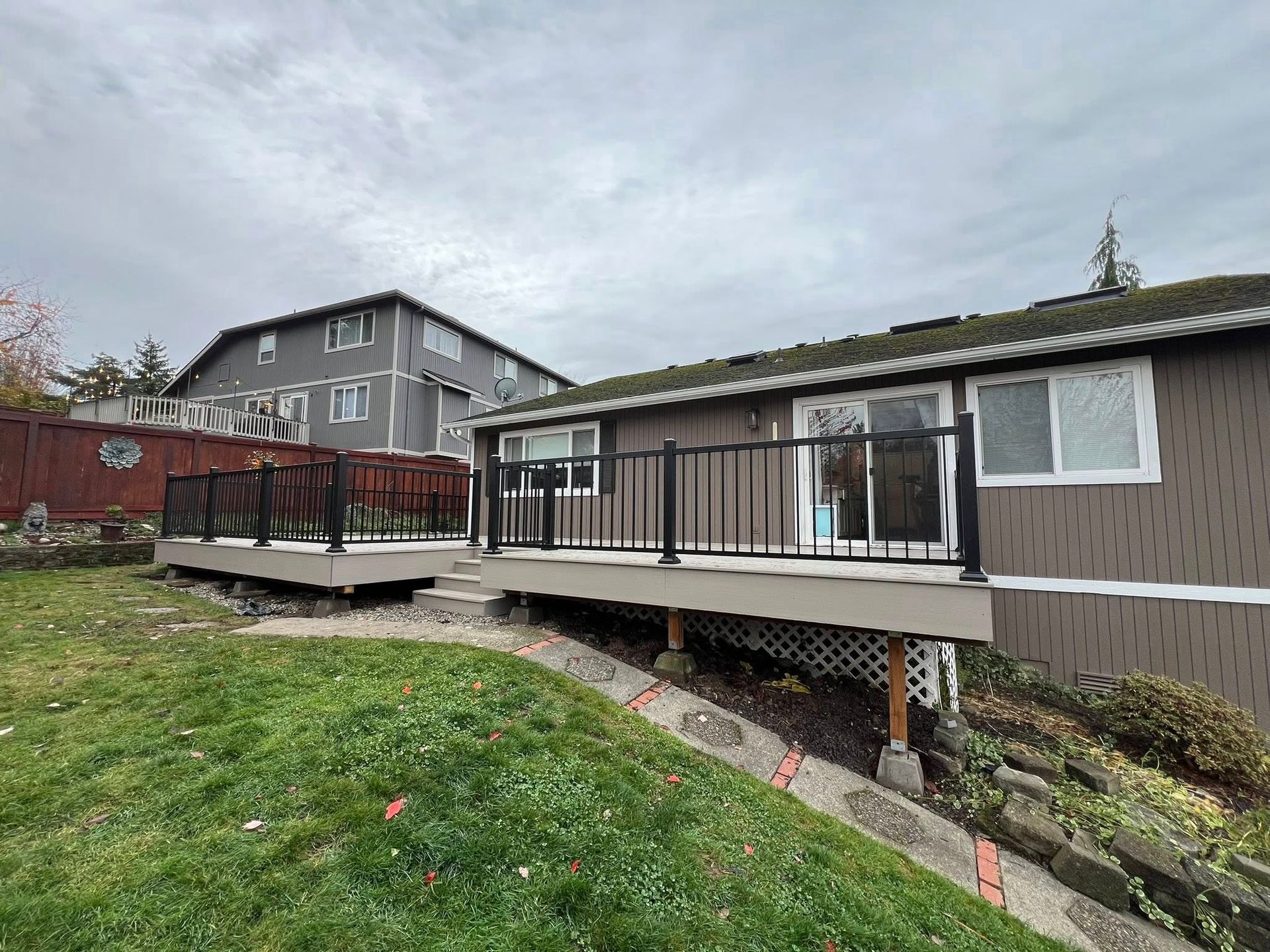 Backyard deck with black railings and a house in the background. Overcast sky, green grass, and brown siding.