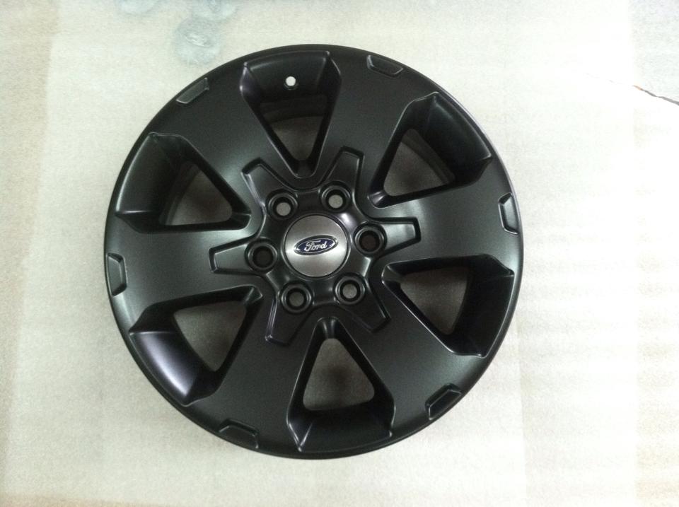 A black ford wheel is sitting on a white surface