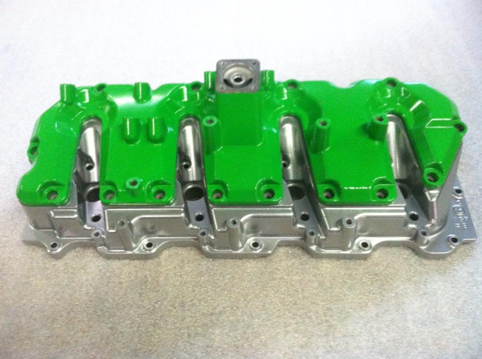 A green and silver engine cover is sitting on a table.