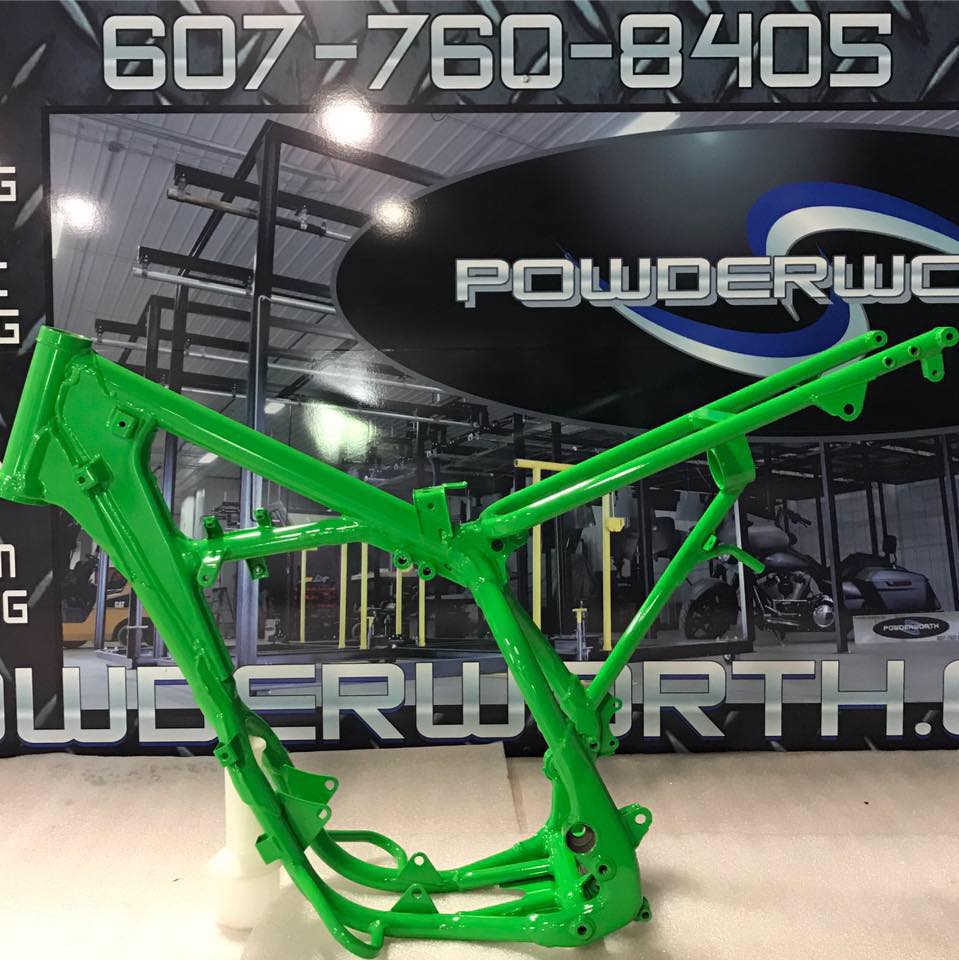 A green motorcycle frame is sitting in front of a sign that says powderwc