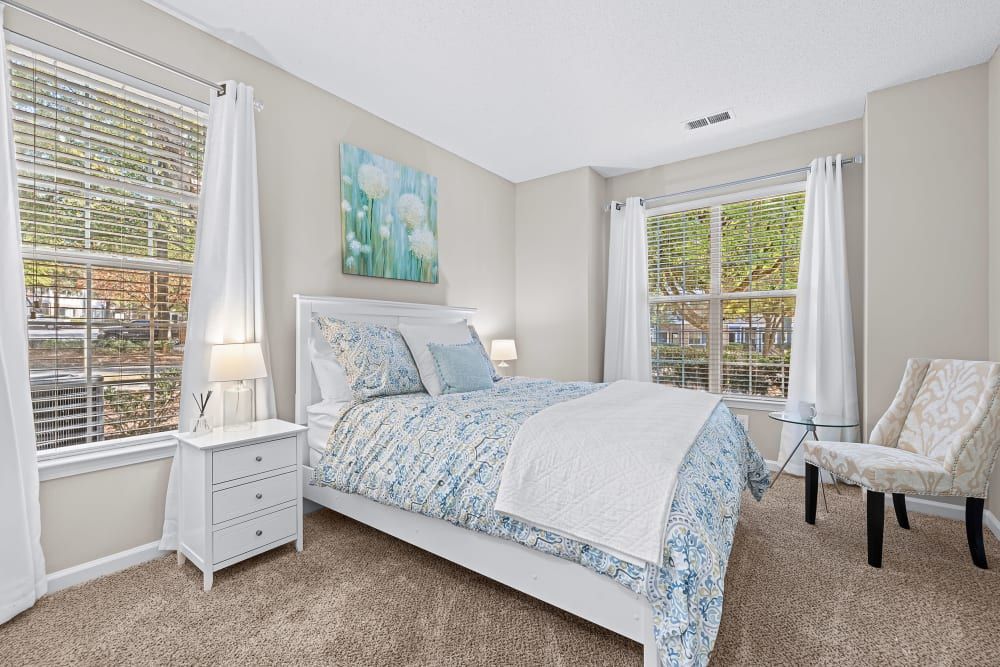 a bedroom with a bed, chair, nightstand, and two windows at Marquis on Edwards Mill in Raleigh, NC. 