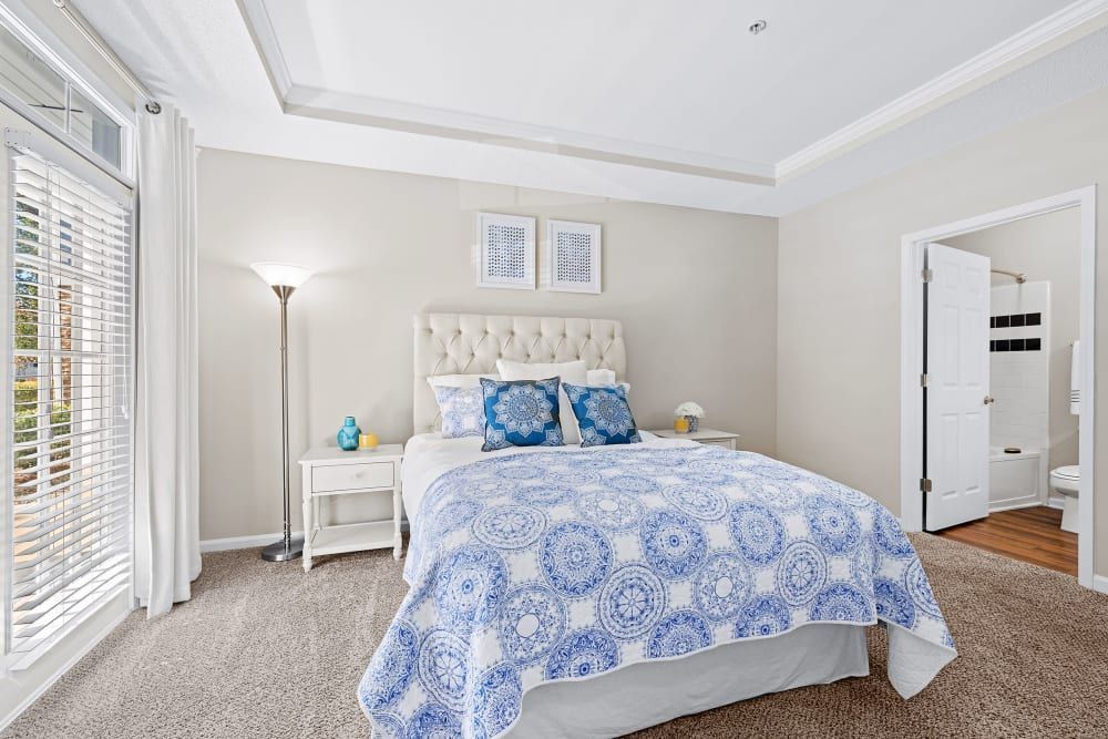 a bedroom with a bed, nightstand, lamp, and sliding glass doors leading to a bathroom at Marquis on Edwards Mill in Raleigh, NC. 
