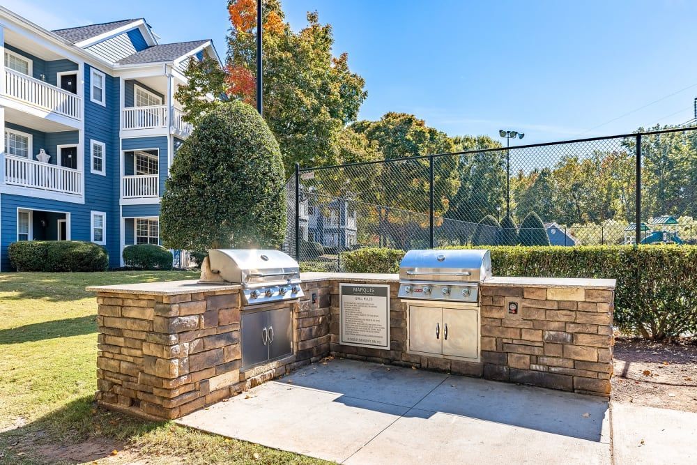 a grill is sitting in front of a building next to a tennis court at Marquis on Edwards Mill in Raleigh, NC. 