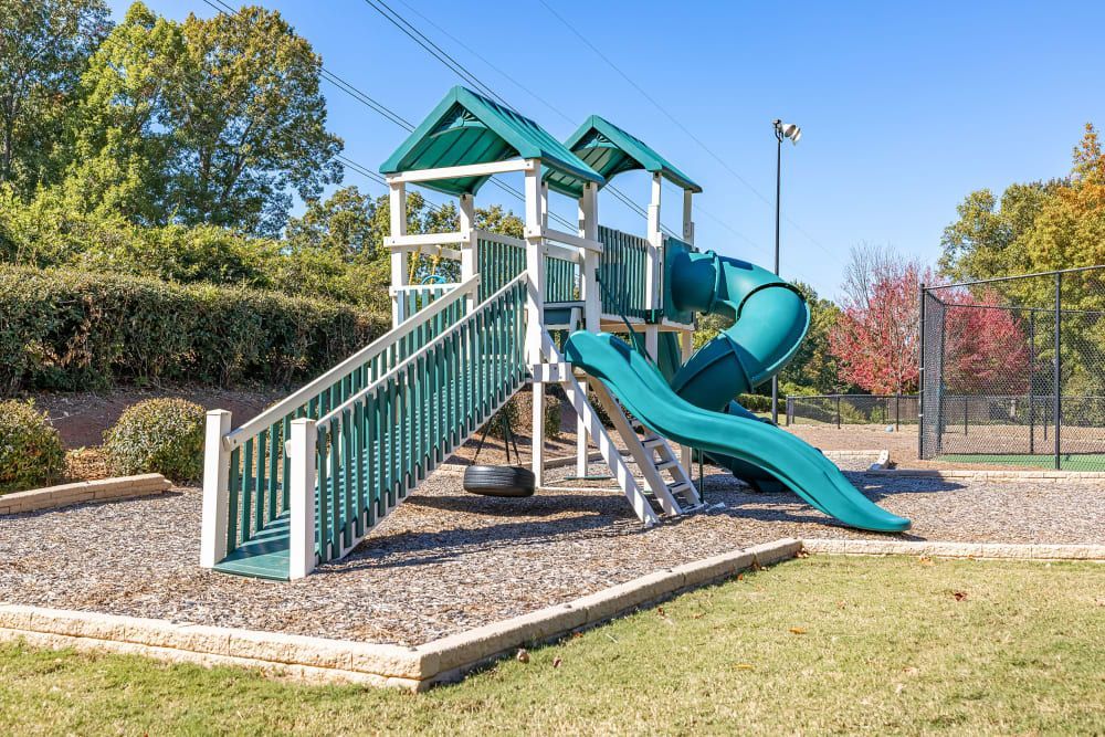 a green and white playground with a slide and swings in a park at Marquis on Edwards Mill in Raleigh, NC. 