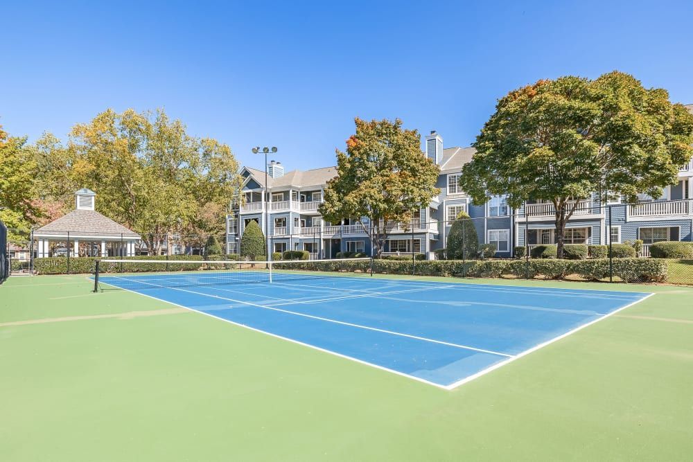 a tennis court with a building in the background and trees in the foreground at Marquis on Edwards Mill in Raleigh, NC. 