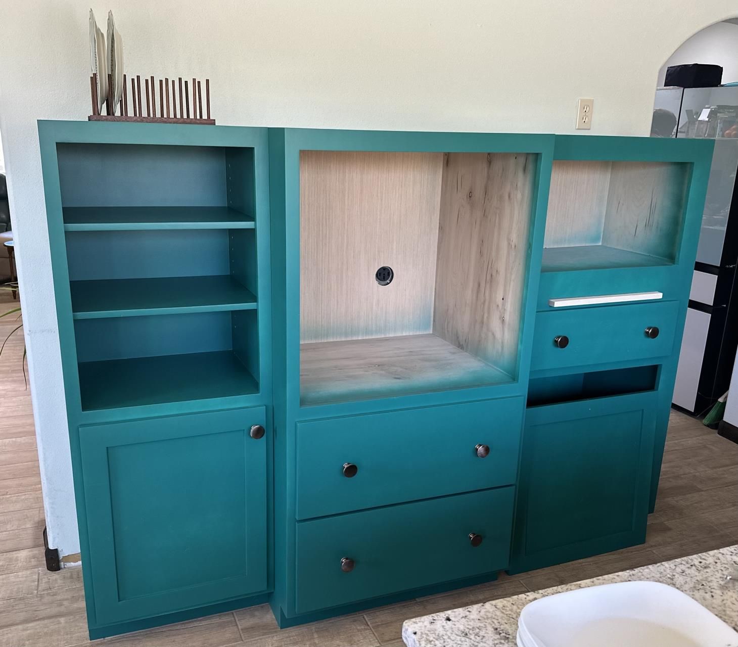 A man is working on a kitchen cabinet with a drill.