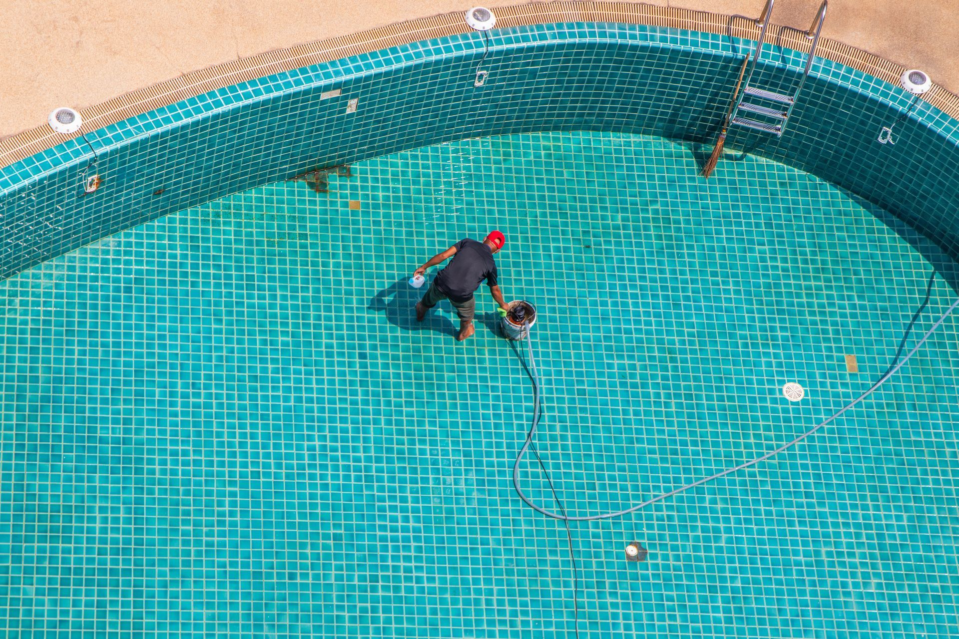 A pool remodeling worker resurfacing a tiled swimming pool.