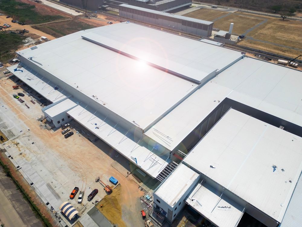 Aerial view of a large industrial building with a silver roof, under construction.