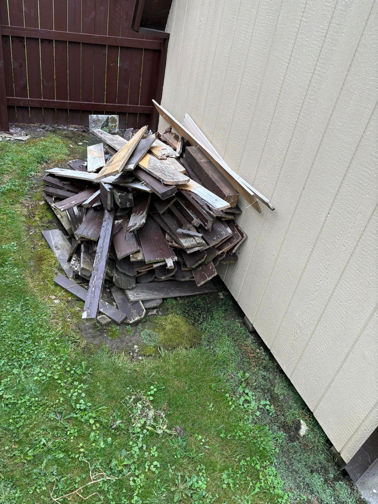 A pile of wood is sitting in the grass next to a building.