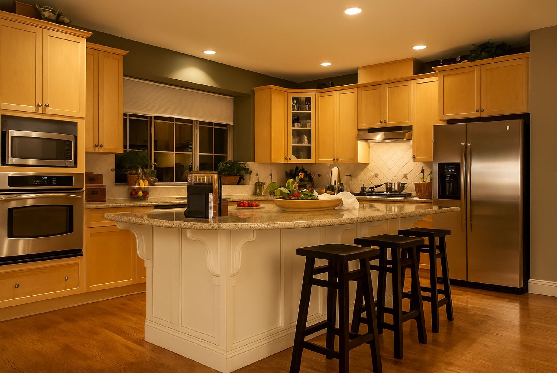 Spacious modern kitchen in a Boise home featuring recessed ceiling lights, a large granite island with barstools, natural wood cabinetry, and stainless steel appliances—lighting installed by A1 Handyman Boise.