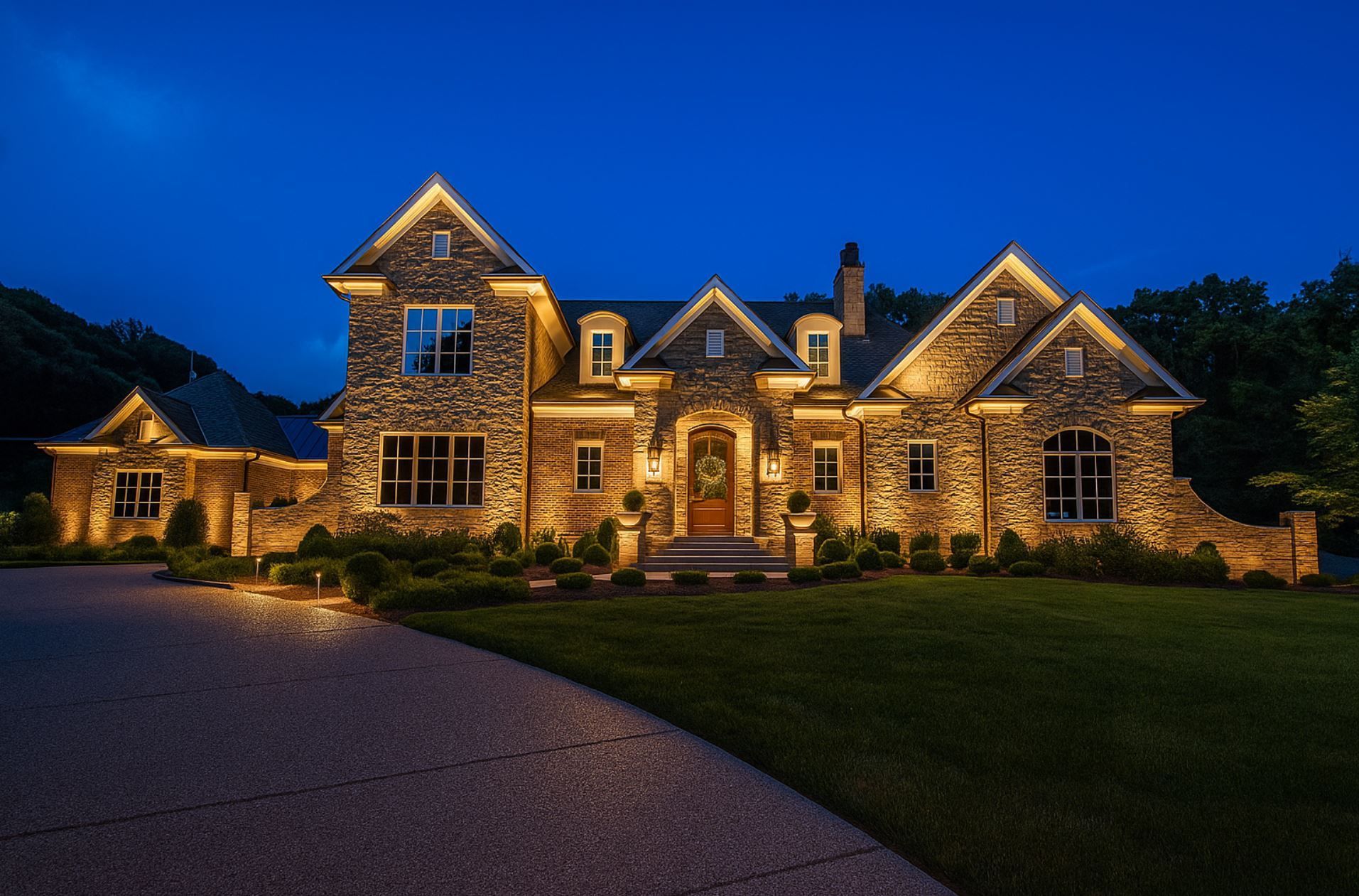 Elegant stone home in Boise with professionally installed outdoor lighting, showcasing landscape uplights and architectural accent lights along the driveway and façade at dusk.