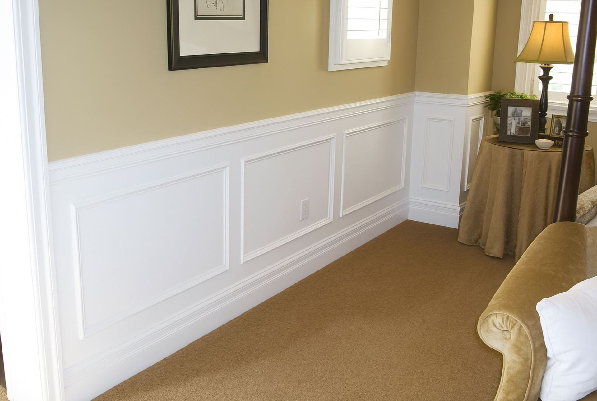 White raised panel wainscoting in a beige living room installed by A1 Handyman, with trim, wall art, and a lamp-lit side table.